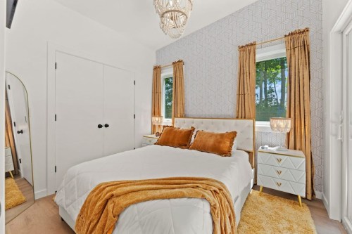 Cozy bedroom with a white bed, gold accents, patterned wallpaper, and large windows with golden curtains.