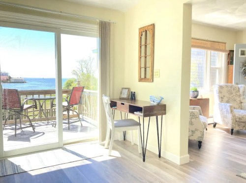 Bright interior with a small desk, overlooking a scenic view of the ocean through sliding glass doors.