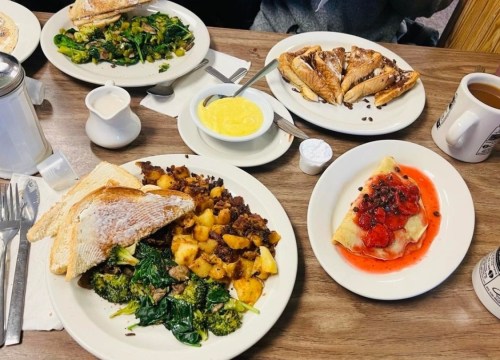 A table set with plates of breakfast: toast, sautéed vegetables, potatoes, pastries, and a bowl of yellow custard.