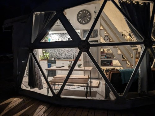 A cozy, modern interior of a geodesic dome at night, featuring a kitchen, dining area, and comfortable seating.