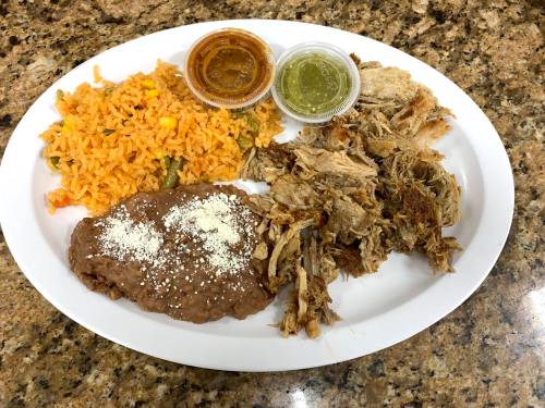 A white plate with rice, refried beans topped with cheese, shredded meat, and two small containers of sauce.