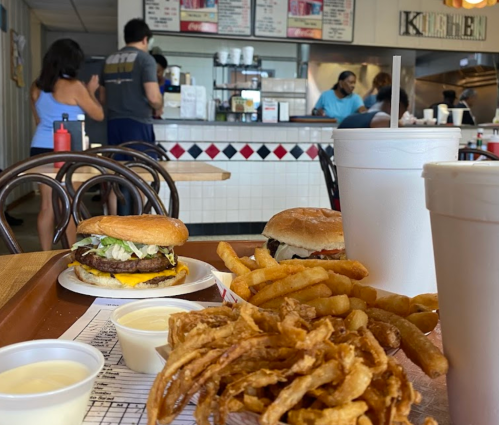 A tray with a burger, fries, and onion rings in a casual diner, with customers in the background.
