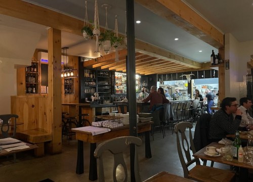 Cozy restaurant interior with wooden beams, bar area, and patrons enjoying their meals in a warm atmosphere.