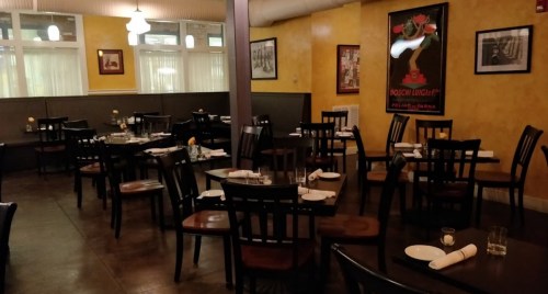 A cozy restaurant interior with wooden tables and chairs, yellow walls, and framed artwork.