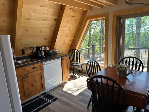 Cozy kitchen with wooden cabinets, a dining table, and large windows overlooking a forested area.