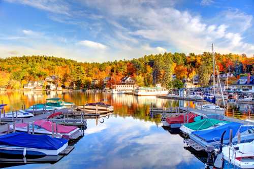 A serene lake scene in autumn, featuring colorful trees, boats in a marina, and a clear blue sky.