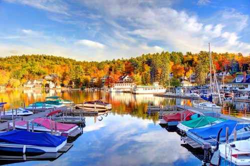A serene lake scene in autumn, featuring colorful trees, boats in a marina, and a clear blue sky.