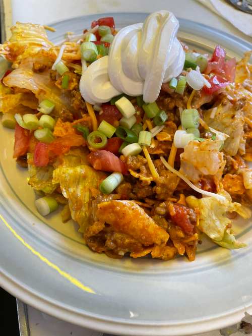 A plate of taco salad with lettuce, tomatoes, cheese, green onions, and a dollop of sour cream on top.