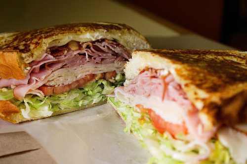 Close-up of a toasted sandwich filled with layers of meats, lettuce, and tomato, cut in half to show the filling.