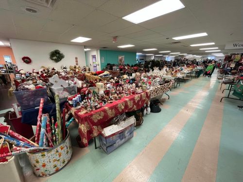 A spacious room filled with tables covered in holiday decorations, gifts, and festive items for sale.
