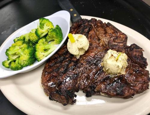 A grilled steak topped with butter, served with a side of steamed broccoli on a white plate.