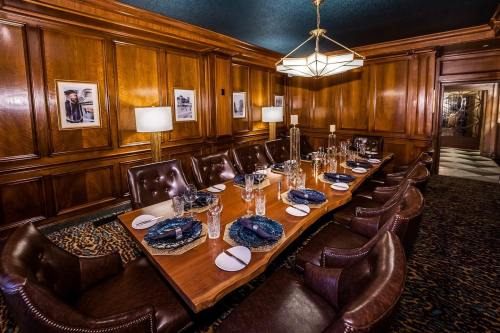 Elegant dining room with a long wooden table set for a meal, surrounded by leather chairs and warm wood paneling.