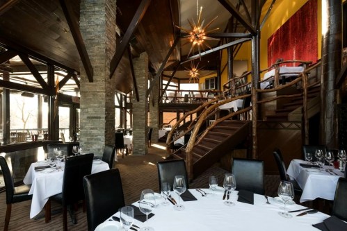 Elegant restaurant interior featuring wooden beams, spiral staircase, and tables set with white linens and glassware.