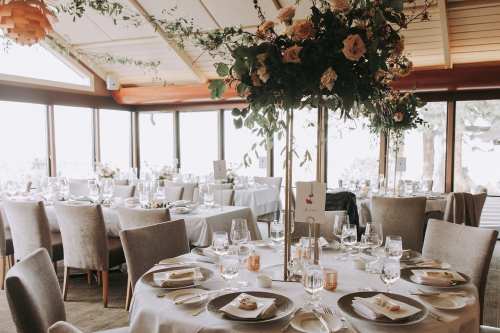 Elegant dining setup with floral centerpieces, glassware, and soft lighting in a bright, airy venue.