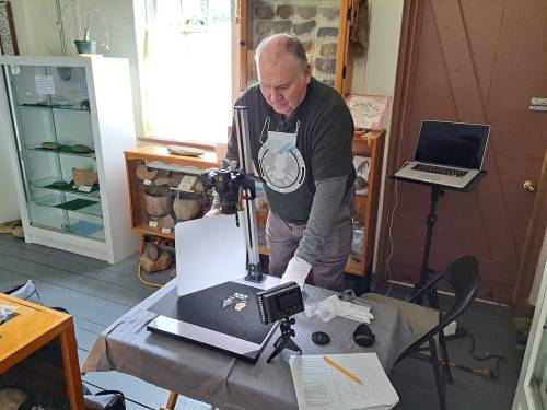 A man sets up a camera and equipment for photographing artifacts in a museum display area.