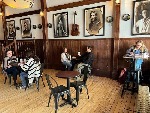 A cozy café with wooden walls, featuring people sitting at tables, enjoying drinks, and studying. Vintage photos adorn the walls.
