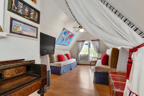 Cozy attic room with a TV, seating area, colorful map, and decorative curtains. Warm wooden floors enhance the inviting space.