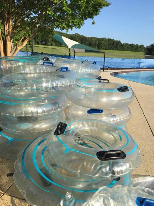 A stack of clear inflatable pool tubes beside a swimming pool on a sunny day.