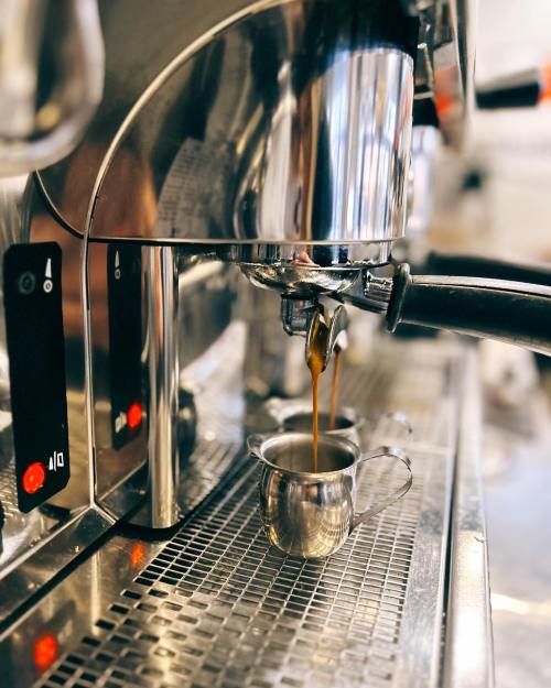 A close-up of an espresso machine brewing coffee into a small metal cup.