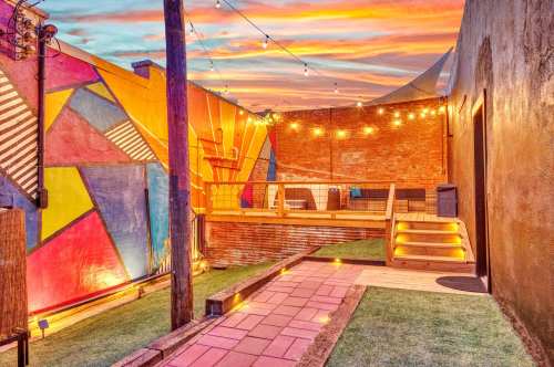 Colorful outdoor space with a vibrant mural, wooden deck, string lights, and a sunset sky.