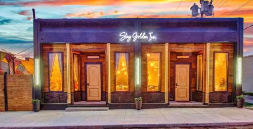 A stylish building with large windows and warm lighting, featuring the sign "Stay Golden Inn" against a colorful sunset sky.