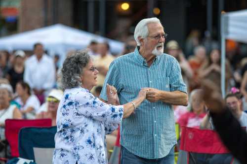 A couple dances together at an outdoor event, surrounded by a crowd enjoying the festivities.