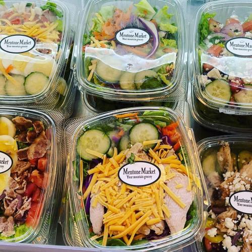 A variety of fresh salads in clear containers, featuring greens, vegetables, and toppings, labeled "Mentone Market."
