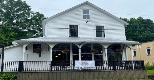 A white, two-story building with large windows and a porch, featuring a sign for "The Hillsboro Pub."