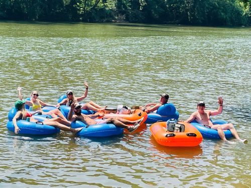 A group of people relaxes on blue and orange inner tubes in a river, enjoying a sunny day.