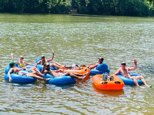 A group of people relaxes on blue and orange inner tubes in a river, enjoying a sunny day.