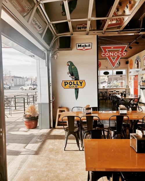 Interior of a diner with a colorful Polly Gas mural, metal chairs, and a view of the street outside.