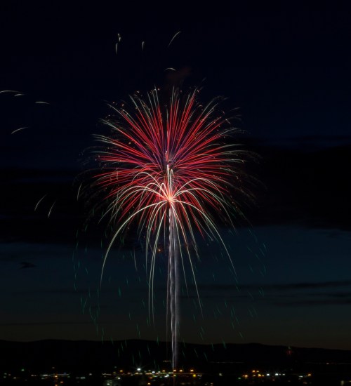 Colorful fireworks burst in the night sky, illuminating the dark backdrop with red, white, and green sparks.