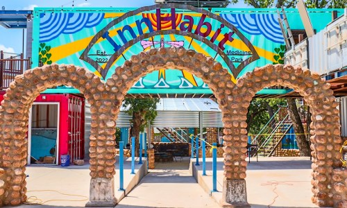 Colorful archway made of stone leads to a vibrant art installation in Medicine Park, with a mural in the background.