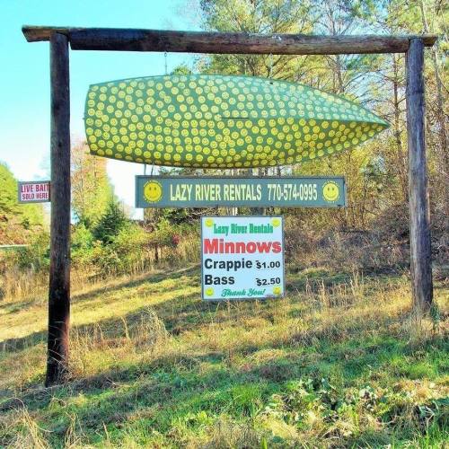 Sign for Lazy River Rentals featuring a large green fish-shaped sign, listing rental prices for minnows and bass.