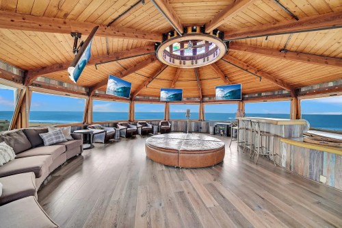 Cozy circular lounge with wooden beams, large windows, and multiple screens, overlooking a scenic ocean view.