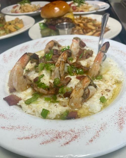 A plate of shrimp and grits topped with green onions and bacon, garnished with paprika.