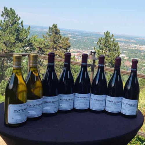 A selection of wine bottles displayed on a table with a scenic view of mountains and a valley in the background.