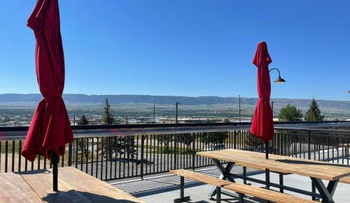 A rooftop patio with red umbrellas, wooden tables, and a scenic view of mountains and blue sky in the background.