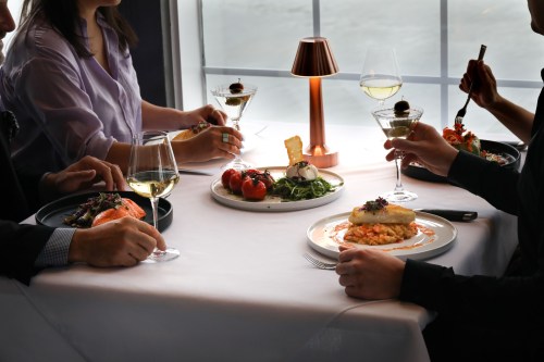 A table set with gourmet dishes, wine glasses, and diners enjoying a meal in a stylish restaurant setting.