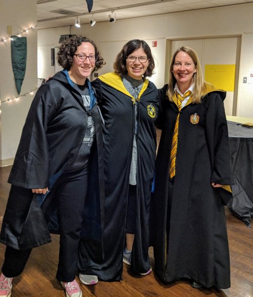 Three women in Hogwarts robes, smiling together, with one wearing a Gryffindor tie and the others in Hufflepuff colors.