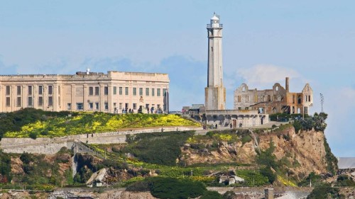 View of Alcatraz Island featuring the historic prison building and lighthouse against a clear blue sky.