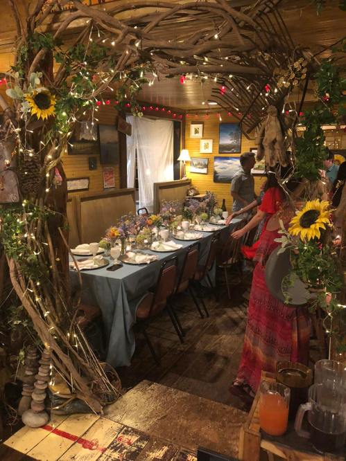 A beautifully decorated dining area with a long table, floral centerpieces, and a rustic archway adorned with lights.