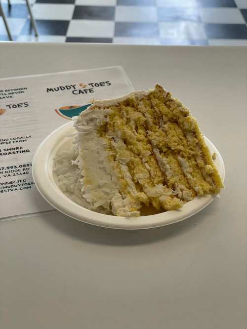 A slice of layered cake with white frosting on a paper plate, next to a menu for Muddy Toes Cafe.