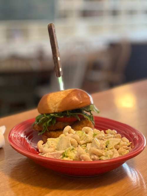 A close-up of a plate featuring a sandwich with greens and a knife, alongside a serving of creamy macaroni salad.