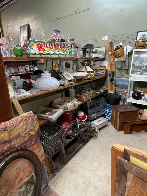 A cozy antique shop display featuring various vintage items, including lamps, glassware, and a billiards sign.
