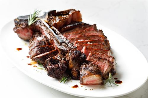 A beautifully cooked steak, sliced and arranged on a white platter, garnished with rosemary and drizzled with sauce.