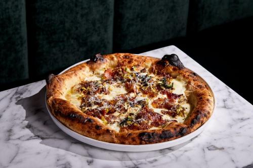 A freshly baked pizza with a golden crust, topped with cheese, herbs, and crispy bits, on a marble table.
