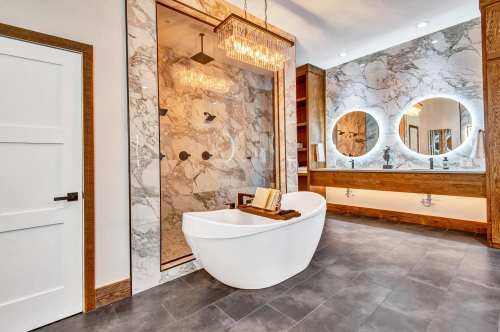Luxurious bathroom featuring a freestanding tub, marble walls, a glass shower, and modern lighting.
