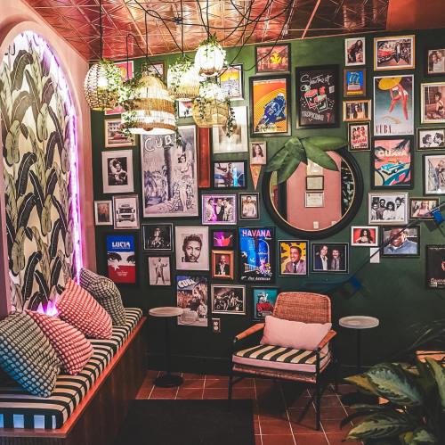 A vibrant lounge with green walls, framed photos, and cozy seating, featuring tropical decor and warm lighting.