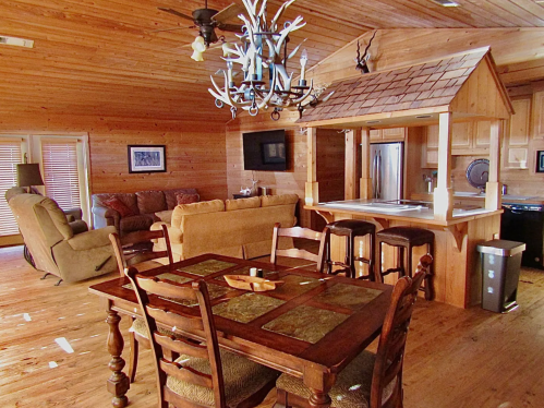 Cozy wooden interior of a cabin featuring a dining table, living area, and kitchen with a rustic design.
